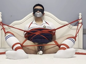 Gay bondage scene with an Asian man tied up and pleasured with a dildo.